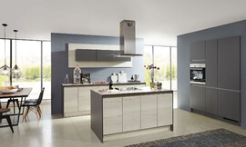 De overgang naar het woondeel bij deze keuken is vloeiend. Deze tijdloze woonkeuken is met greeploze fronten in vriendelijk houtoptiek en een keukeneiland uitgerust. Zuordnung: Stil Design-keukens, Planungsart keukenblok