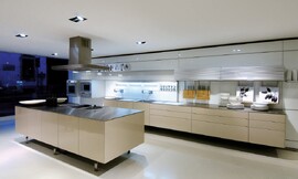 Design keuken met erg dunne greeploze fronten en aanrechtbladen. Het kookeiland staat op poten en heeft een kookveld, hier met stoomkoker uitgevoerd. Verlichting met spots in het plafond. Zuordnung: Stil Design-keukens, Planungsart Binneninrichting van de keuken