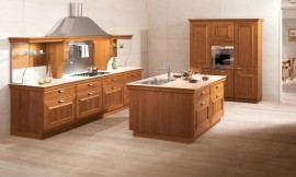 Landelijke keuken met warme houttinten en cassettefronten. Een keukeneiland met wasbak maakt deze keuken open en communicatief. De belangrijkste keukenwand heeft een brede afzuigkap in een riante schouw en planken van glas voor servies. Zuordnung: Stil Landelijke keukens, Planungsart Keuken met keukeneiland