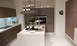 U-vormige keuken met kookeiland in het midden. Mat grijze fronten en witte aanrechtbladen. De inductie-kookplaten bevinden zich op het kookeiland voor een praktische workflow. Zuordnung: Stil Design-keukens, Planungsart keukenblok
