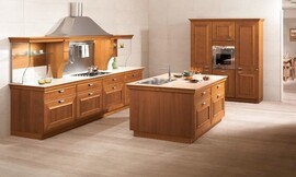 Landelijke keuken met warme houttinten en cassettefronten. Een keukeneiland met wasbak maakt deze keuken open en communicatief. De belangrijkste keukenwand heeft een brede afzuigkap in een riante schouw en planken van glas voor servies. Zuordnung: Stil Landelijke keukens, Planungsart Open keuken (woonkeuken)