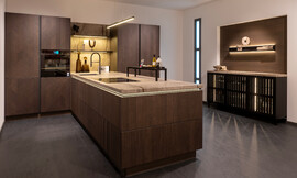 Een perfecte mix van tijdloze moderniteit en hoge functionaliteit. Deze greeploze keuken biedt een L-vormige planning en een elegant donker hout frontdecor met steen aanrecht. Zuordnung: Stil Moderne keukens, Planungsart Keuken met zitgelegenheid