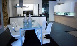 Zwart-witte keuken met greeploze fronten en blauwe verlichting in de sokkel. Hier ziet u de bijbehorende eettafel met glazen tafelblad en design stoelen. Zuordnung: Stil Design-keukens, Planungsart Open keuken (woonkeuken)