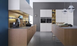 Deze keuken die uit drie elementen bestaat biedt een  combinatie van bijzonder natuurlijk werkende kopereiken fronten met matte sahara-lak oppervlakken. Het eerste keukenblok bevat het fornuis en de spoelbak. De kopereiken onderkasten zijn zwevend aangebracht. Daarboven hangen de bovenkasten in een witte kleur. In de hangkast is een efficiëntie afzuigkap geïntegreerd die geen luchtafvoer behoeft. Perfecte plaats om te werken in de keuken biedt het keukeneiland. Dit eiland is ook van kopereiken en staat op drie open metalen poten. Het andere wandblok, in dezelfde lichte kleur als de hangkasten, is hoog en biedt behalve veel bergruimte ook de nodige apparatuur. Midden in het hoge keukenblok bevindt zich een open kast, waar weer de kopereiken tint in terugkomt. Al met al een moderne keuken met een harmonische en rustige uitstraling met voldoende berg- en werkruimte. Zuordnung: Stil Moderne keukens, Planungsart U-vormige keuken
