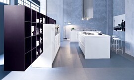 In deze moderne witte keuken wordt het accent gezet door de paarse open kast die op de half hoge apparatuurkasten steunt. Evenals de apparatuurkasten is het kookeiland glanzend wit en strak vormgegeven. Boven het fornuis is vanaf het plafond een moderne designafzuigkap bevestigd met eveneens een zeer strakke vormgeving. De zitgelegenheid die aan de andere kant van het kookeiland is ontstaan, maakt koken tot een sociale belevenis. Het derde keukenblok bestaat uit alleen maar onderkasten. De spoelbakken zijn ook in dit gedeelte van de keuken opgenomen. 

Een kastenwand met apparatuur en opbergruimte gecombineerd met een keukeneiland met fornuis en zitgelegenheid voor een sociale kookbeleving. Stijl: design. Witte meubels en aanrechtbladen, daaromheen een paarse kast (open). Zuordnung: Stil Moderne keukens, Planungsart Keuken met keukeneiland