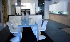 Zwart-witte keuken met greeploze fronten en blauwe verlichting in de sokkel. Hier ziet u de bijbehorende eettafel met glazen tafelblad en design stoelen. Zuordnung: Stil Moderne keukens, Planungsart U-vormige keuken