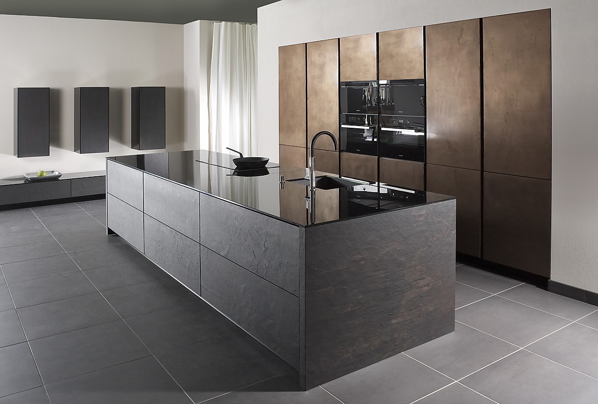 De open ontworpen, representatieve luxe keuken biedt maximale functionaliteit met veel bergruimte. Voor het kookeiliand is gebruik gemaakt van echte grijze leisteen. Het dunne, hoogglanzende aanrechtblad zorgt voor een interessant contrast. Op het kookeiland zijn de spoelbak en het fornuis opgenomen. In de wand zijn in hoge kasten de apparaten opgenomen, twee daarvan op een praktische werkhoogte. De luxe en exclusieve uitstraling van deze greeploze keuken wordt door niets verstoord. Zuordnung: Stil Luxe keukens, Planungsart Keuken met keukeneiland