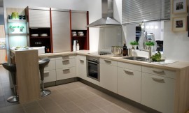 Deze gezellige L-vormige keuken biedt zeven onderkasten met beige structuurlak. Op het stompe gedeelte van de L-vorm zijn drie opzetkasten geplaatst die voorzien zijn van praktische rolluiken. Aan dit gedeelte sluit een bar in houtoptiek aan, zodat hier een zitgelegenheid voor twee personen wordt geboden. Het fornuis, de oven en de spoelbak zijn opgnomen in het langere gedeelte van de L-vorm. Zuordnung: Stil Moderne keukens, Planungsart keukenblok