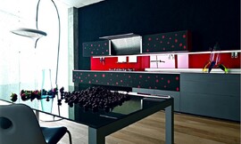 Design keuken van gerecycled glas. Greeploze grijze en zwarte fronten met rode stippen, felrode keukenachterwand. De afzuigkap zit in de bovenkast ingebouwd en kan open- en dichtgeklapt worden. Deze keuken laat zien wat fronten met creatieve opdruk voor het totaalbeeld kunnen betekenen. Zuordnung: Stil Design-keukens, Planungsart Detail keukenontwerp
