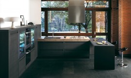 Overzichtelijke keuken in U-vorm met contrast tussen mat-donkere meubels en robuust aanrechtblad. Design fronten met greeplijst. Met simpele bar en zitgelegenheid voor interactie tijdens het koken. Design afzuigkap in het plafond. Zuordnung: Stil Moderne keukens, Planungsart Detail keukenontwerp