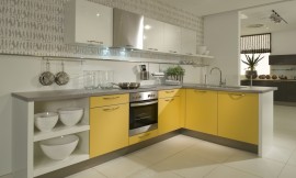 L-vormige keuken met mango gele en witte fronten en een grijs granieten aanrechtblad. De afzuigkap past onopvallend tussen de andere bovenkasten en de spoelbak op het uitstekende keukenblok is voorzien van een glasplaat om spetters tegen te houden. Zuordnung: Stil Moderne keukens, Planungsart Detail keukenontwerp
