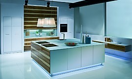 Deze keuken is een voorbeeld van het gebruik van hout in de design context. Het sterke contrast tussen het amber patroon en de lichtblauwe, strakke keukenfronten is een lust voor het oog. Een dun aanrechtblad draagt bij aan deze compositie. Boven het keukeneiland is een afzuigkap in een lampenkap aangebracht. Zuordnung: Stil Luxe keukens, Planungsart Keuken met keukeneiland