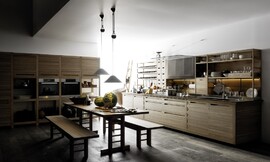 Designkeuken bestaande uit twee keukenblokken met landelijke accenten: houttinten, brede grepen, houten rekken/kasten en in het midden van de keuken een traditionele houten tafel met banken. Op het ene keukenblok, waarin zich ook de spoelbak en het fornuis bevinden, zijn half open kasten geplaatst die ideaal zijn voor het opbergen van het serviesgoed of decoratieve accessoires. Het andere keukenblok bestaat uit hoge kasten die voor een deel open zijn en daardoor aan stellingskasten doen denken. In het midden van de hoge kasten is op praktische werkhoogte de roestvrijstalen apparatuur naast elkaar aangebracht. Zuordnung: Stil Design-keukens, Planungsart Keuken met keukeneiland