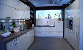 Deze moderne U-vormige keuken heeft hoogglans fronten in de kleur magnolia en een lichtbak tegen de achterwand. Aanrechtbladen in een donkerbruine houttint. De kastenwand rechts biedt veel opbergruimte. Zuordnung: Stil Moderne keukens, Planungsart Detail keukenontwerp