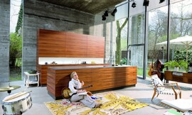 Deze keuken met vlakke houtesthetiek valt op door gebrek aan grepen en zijn slanke aanrechtbladen. Optisch wordt het beeld gedomineerd door de prachtige horizontale tekening van het hout. De keuken roept een loungy sfeer op. Zuordnung: Stil Moderne keukens, Planungsart Keuken met keukeneiland