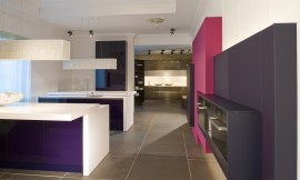 Moderne keuken met meerdere roze- en paarstinten. Twee kookeilanden met bar. Hangende lampen van wit geschilderd riet. Rechts ziet u een concept voor inbouwapparatuur waarbij de apparaten in een dunne kast ingebouwd zijn en daardoor in de ruimte lijken te hangen. Zuordnung: Stil Design-keukens, Planungsart Keuken met keukeneiland