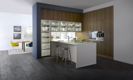 Een harmonieuze drieklank van materialen: keukenfronten met natuurlijk werkend houten structuuroppervlakte, matte magnolia kunststof en een dun wit aanrechtblad/keukenblok. Glazen deurtjes voor de servieskast maken het geheel af. Zuordnung: Stil Klassieke keukens, Planungsart Open keuken (woonkeuken)