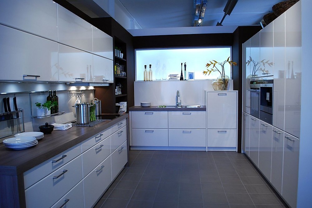 Deze moderne U-vormige keuken heeft hoogglans fronten in de kleur magnolia en een lichtbak tegen de achterwand. Aanrechtbladen in een donkerbruine houttint. De kastenwand rechts biedt veel opbergruimte. Zuordnung: Stil Moderne keukens, Planungsart U-vormige keuken