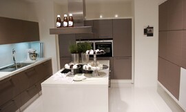 U-vormige keuken met kookeiland in het midden. Mat grijze fronten en witte aanrechtbladen. De inductie-kookplaten bevinden zich op het kookeiland voor een praktische workflow. Zuordnung: Stil Design-keukens, Planungsart Keuken met keukeneiland
