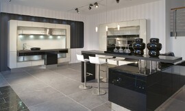 Open eilandkeuken met een speelse, afgeronde vormentaal en een retro randje. Zowel de keukenkast rechts als het werkgedeelte links zijn versierd met een smal, afgerond kader. Een bar die vanuit een onderkast de kamer in beweegt biedt zitgelegenheid in deze communicatieve keuken. Zuordnung: Stil Moderne keukens, Planungsart Keuken met keukeneiland