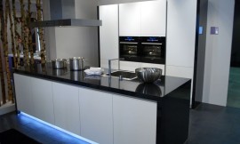 Design keuken met hoogglans zwarte wangen en aanrechtblad. Greeploze fronten en opvallende blauwe verlichting uit de sokkel van het keukeneiland. Zuordnung: Stil Moderne keukens, Planungsart Open keuken (woonkeuken)