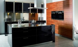 Deze keuken bestaat uit twee keukenblokken die tegen de wand geplaatst zijn en een apart kookeiland. In een van de twee keukenblokken met het natuurlijke tineo fineer, met duidelijke houtstructuur, is de apparatuur op praktische werkhoogte opgenomen. Het kookeiland en het andere keukenblok zijn voorzien van een in 13 stappen vervaardigde zwarte hoogglans lak, waardoor een spannend contrast met de houtoptiek van de hoge apparatuurkasten is ontstaan. Het roestvrij staal van de sokkels komt weer terug in de vijf hangkasten boven de spoelbak, die samen met de onderkasten en de grote lades voor voldoende bergruimte zorgen. Zuordnung: Stil Design-keukens, Planungsart keukenblok