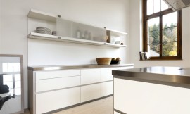 Deze moderne witte designkeuken maakt met zijn roestvrijstalen aanrechtbladen en greeploze witte fronten een strakke indruk. Aan de wand is een keukenblok geplaatst met grote, praktische lades. De lage kast daarboven heeft verschuifbare matglazen fronten en is voor een deel open. Het kookeiland heeft hetzelfde design: roestvrijstalen werkblad, witte greeploze fronten. Niets verstoort hier de kalmte die deze keuken uitstraalt. Zuordnung: Stil Design-keukens, Planungsart Keuken met keukeneiland