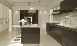 Keuken met indrukwekkende hoogglans fronten en keukeneiland met wit aanrechtblad en hoge bar met zitgelegenheid op barkrukken. De grote, ongebroken sepia bruine vlakken van de greeploze fronten geven deze keuken een krachtig timbre. Zuordnung: Stil Moderne keukens, Planungsart Keuken met keukeneiland