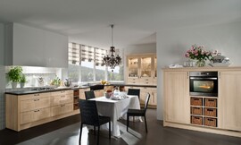 Hier ziet u een landelijke keuken in een L-opstelling met een extra blok met half hoge kasten. De kaderfronten met lichte houttint en de vakken met manden versterken het landlijke effect van deze keuken. De vier grote en twee normale lades onder het fornuis bieden genoeg plaats voor het kookgerei. In hetzelfde deel van de keuken bevindt zich ook de spoelbak. In het andere deel van de L-opstelling zijn er opzetkasten geplaatst, die de landelijke keuken ook een klassieke touch geven. De oven en koelapparatuur zijn opgenomen in de halfhoge kasten. Zuordnung: Stil Landelijke keukens, Planungsart L-vormige keuken