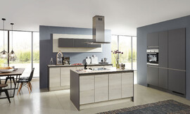 De overgang naar het woondeel bij deze keuken is vloeiend. Deze tijdloze woonkeuken is met greeploze fronten in vriendelijk houtoptiek en een keukeneiland uitgerust. Zuordnung: Stil Moderne keukens, Planungsart U-vormige keuken