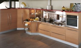 Keuken met houten fronten en lange grepen. Aanrechtblad in speelse, golvende vorm. Stalen achterwand bij het werkgedeelte. Een rode lijst (boven) verbindt de verschillende gedeeltes van de keuken optisch. Zuordnung: Stil Landelijke keukens, Planungsart Keuken met keukeneiland