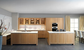 Moderne landelijke keuken met gebeitst eiken fineer &quot;tonnato&quot; en nette witte aanrechtbladen. Het grootste keukenblok is tegen de wand geplaatst en biedt in de lades veel bergruimte. Daarboven hangen kastjes met glazen deuren, zo kan het mooie servies ook als decoratie-object worden gebruikt. Op de legplanken in de nis is er plaats voor de mooiste glazen en andere accessoires. Rechts zijn de hoge apparatuurkasten opgenomen. De keuken beschikt verder nog over twee eilanden. Op het ene keukeneiland is de dubbele spoelbak met praktische handdouche opgenomen. Het aanrechtblad steekt hier iets uit, zodat er door de daar geplaatste bank een fraaie zitgelegenheid is ontstaan. Op het andere eiland kan er gekookt worden. Zuordnung: Stil Landelijke keukens, Planungsart L-vormige keuken