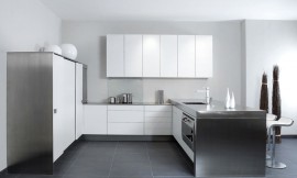 Elegantie ontmoet modernisme: geborsteld pijnhout met kokoswit glazuur, gecombineerd met koel roestvrij staal. Het aanrechtblad rechts verschilt in hoogte met de rest van het werkbereik. De keukenkastjes vallen op door hun relatief smalle deurtjes. Zuordnung: Stil Design-keukens, Planungsart Keuken met zitgelegenheid