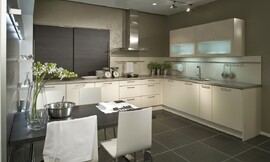 U-keuken met een aparte eettafel. Simpele fronten, gebroken wit met grepen. Wandkast met grotere panelen van donker hout. Een relatief dun granieten aanrechtblad maakt de keuken af. Zuordnung: Stil Moderne keukens, Planungsart Detail keukenontwerp