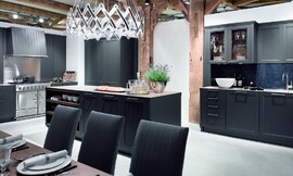 Deze open keuken heeft matzwarte kader fronten met grepen en een dun aanrechtblad. Passend is ook de bovenkast met glazen deurtjes. Hier uitgevoerd met een luxe fornuis. Zuordnung: Stil Landelijke keukens, Planungsart Open keuken (woonkeuken)