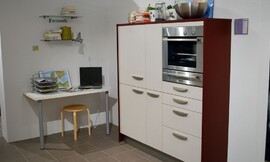 Voorbeeld van een werkplek in de hoek van de keuken. Een simpel tafelblad aan de muur met twee tafelpoten. Keukenkast met gebroken witte fronten en wangen van donker hout. Ingebouwde magnetron-oven-combinatie. Zuordnung: Stil Moderne keukens, Planungsart Open keuken (woonkeuken)