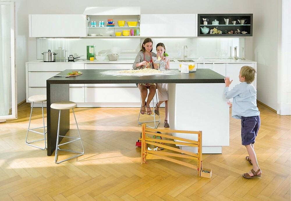 Deze familiekeuken bestaat uit een breed keukenblok met hangkasten en een simpel kookeiland met zitgelegenheid. Witte fronten met brede greeplijst. Bovenkast met zich naar boven openende kleppen. Zuordnung: Stil Moderne keukens, Planungsart keukenblok