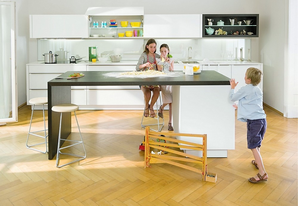 Deze familiekeuken bestaat uit een breed keukenblok met hangkasten en een simpel kookeiland met zitgelegenheid. Witte fronten met brede greeplijst. Bovenkast met zich naar boven openende kleppen. Zuordnung: Stil Moderne keukens, Planungsart keukenblok
