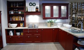 Landelijke keuken met cassette fronten (knopgrepen) in de bijzondere kleur indisch rood. Het aanrechtblad in lichtere tint contrasteert met de rest van de keuken. Bovenkasten met matglazen deurtjes. Links is open opbergruimte te vinden. De afzuigkap is ingebouwd in een schouw. Zuordnung: Stil Moderne keukens, Planungsart keukenblok