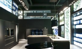 Design eilandkeuken met bijzondere afzuigkap/verlichting en een rond, zwart bartafeltje. Grijze fronten met greeplijsten. Aanrechtblad lichte tint, komt visueel los van het keukeneiland. Zuordnung: Stil Design-keukens, Planungsart Keuken met keukeneiland