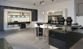 Open eilandkeuken met een speelse, afgeronde vormentaal en een retro randje. Zowel de keukenkast rechts als het werkgedeelte links zijn versierd met een smal, afgerond kader. Een bar die vanuit een onderkast de kamer in beweegt biedt zitgelegenheid in deze communicatieve keuken. Zuordnung: Stil Moderne keukens, Planungsart Keuken met keukeneiland