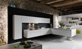 In deze moderne zwevende designkeuken komt de L-vorm twee keer terug. Eén keer als hoge kast tegen de muur met twee brede bovenkasten daarnaast. Ook het ondergedeelte vormt een L. Op het ene gedeelte van de L kan er worden gekookt, de afzuigkap is in de kast daarboven vrijwel onzichtbaar opgenomen. Het andere deel van de L is o.a. voorzien van de spoelbak. De greeploze strakke kasten en het dunne aanrechtblad zorgen voor een rustige uitstraling. Zuordnung: Stil Luxe keukens, Planungsart Keuken met keukeneiland