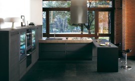 Overzichtelijke keuken in U-vorm met contrast tussen mat-donkere meubels en robuust aanrechtblad. Design fronten met greeplijst. Met simpele bar en zitgelegenheid voor interactie tijdens het koken. Design afzuigkap in het plafond. Zuordnung: Stil Moderne keukens, Planungsart Keuken met keukeneiland