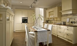 In deze keuken ziet u enkele typische ornamenten toegepast in landelijke keukens. Behalve cassette fronten ziet u bijvoorbeeld een schouw, opvallende sokkels en afgeronde lijsten aan de bovenkanten van de meubels. Hier uitgevoerd met een passende eetkamertafel. Zuordnung: Stil Landelijke keukens, Planungsart Keuken met keukeneiland