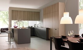 Dit simpele, rechtlijnige ontwerp bereikt een rustige werking van de ruimte. De verschillende tinten (licht hout, donkerbruin, mat zwart) zijn op gewaagde wijze ingezet met een sensibel resultaat: een bijzonder harmonieuze keuken. Een klein aanrechtblad dat over de rand van het keukeneiland uitsteekt creëert een zitgelegenheid. Zuordnung: Stil Moderne keukens, Planungsart Open keuken (woonkeuken)