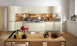 Moderne, deels greeploze keuken bestaande uit een brede, symmetrische keukenwand. Beige fronten contrasteren met metaaltinten en licht hout. Speels, golvend ontwerp. Een bijzondere tafel met smalle plankjes maakt het geheel af. Zuordnung: Stil Moderne keukens, Planungsart keukenblok