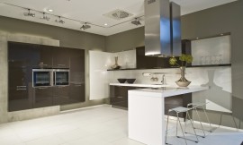 Deze moderne keuken leunt optisch op het contrast tussen sepia bruine kasten en een wit aanrechtblad, bar en achterwand. De apparatuurkast links is zwevend gemonteerd tegen een grijze strook. Zuordnung: Stil Moderne keukens, Planungsart U-vormige keuken