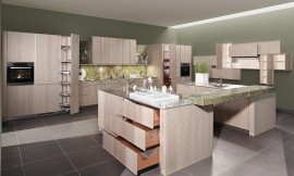 Moderne behaaglijkheid en absolute elegantie. Het oppervlakte is gebeitst in de tint &quot;zilver eik&quot;, waardoor deze topkeuken herinnert aan de natuurlijkheid van oude versleten houtplanken. Het binnenwerk van de lades in massief notenhout biedt een aangenaam, warm contrast met de koelere tint van de buitenkant van de meubels. Zuordnung: Stil Moderne keukens, Planungsart L-vormige keuken