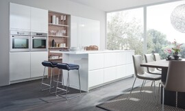 De stralend &quot;firn&quot;-witte hoogglans gelakte fronten hebben ergonomische greeplijsten in plaats van zichtbare grepen. Doordat het aanrechtblad van het keukeneiland uitsteekt ontstaat zitgelegenheid op barkrukken. De kastenwand is in de muur verzonken. Zuordnung: Stil Design-keukens, Planungsart Detail keukenontwerp