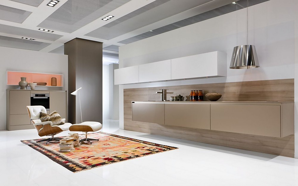 Deze zwevende keuken heeft naast aan de wand hangende witte bovenkasten ook beige hangende onderkasten. De oven is op praktische werkhoogte opgenomen in de half hoge beige kasten. Greeploos en met strakke vormgegving valt deze ruimte nauwelijks meer te herkennen als keuken en zorgt voor een symbiotische overgang van keuken naar woonkamer. Zuordnung: Stil Design-keukens, Planungsart Open keuken (woonkeuken)